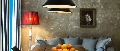 A wooden dining table with a basket of apples, a red lamp, and a painting on the wall.