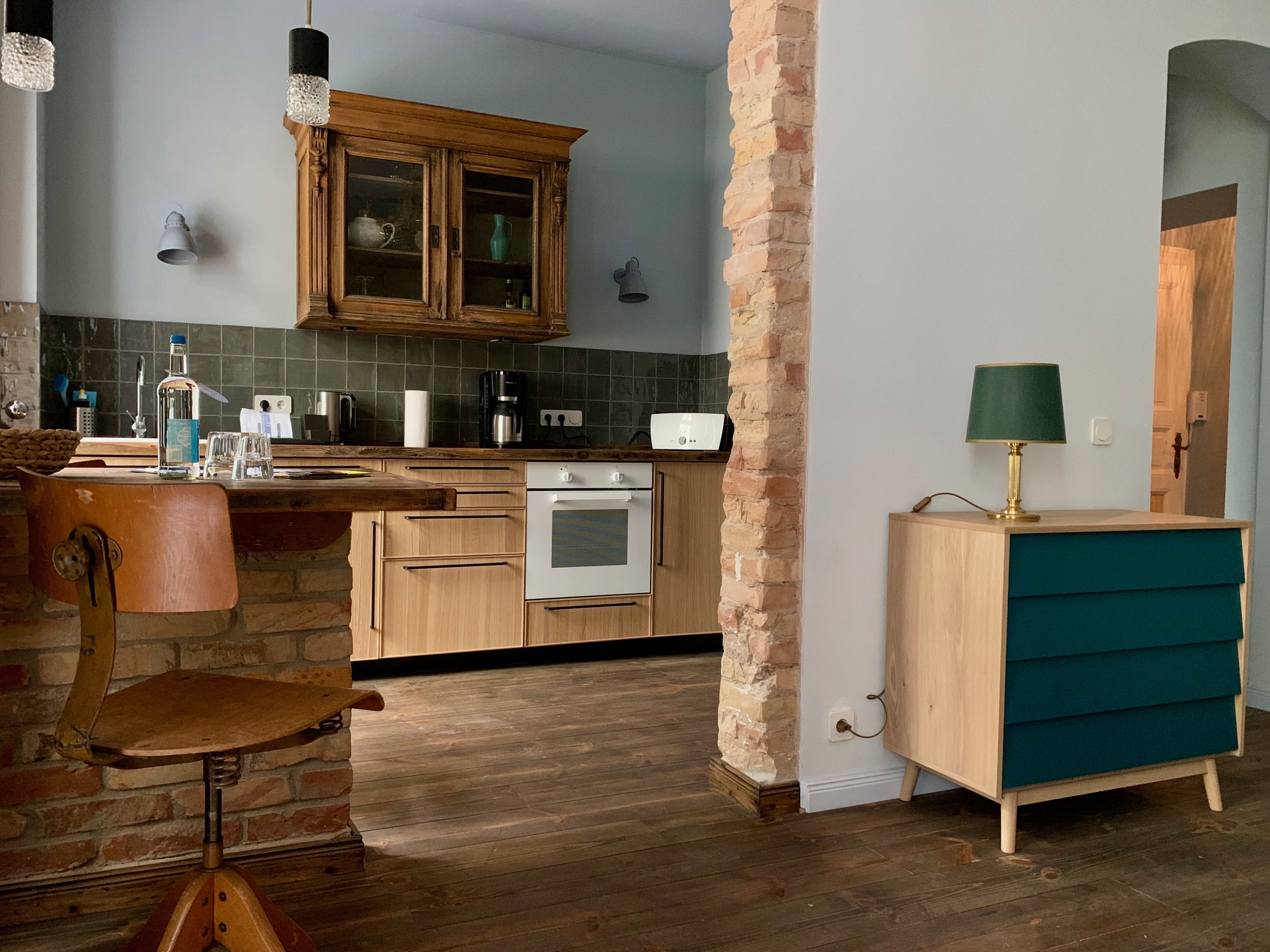 A kitchen with wooden cabinets, a brick column, a wooden chair, and a teal-colored cabinet.