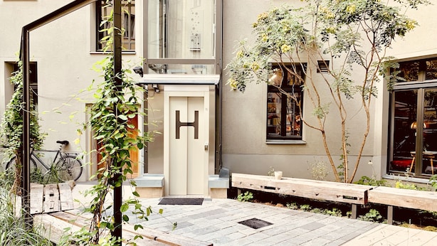 Un patio con un banco de madera, una bicicleta y un edificio con una H grande en la puerta.