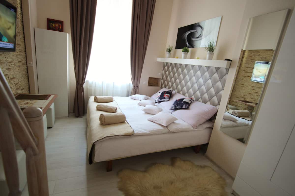 A modern bedroom with a bed, a mirror, a dresser, and a television on the wall.
