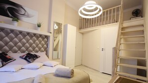 A modern hotel room with a tufted headboard, a large bed, a built-in wardrobe, a wooden ladder, and a ceiling light fixture. - Rainbow Apartments 2 (Kraków)