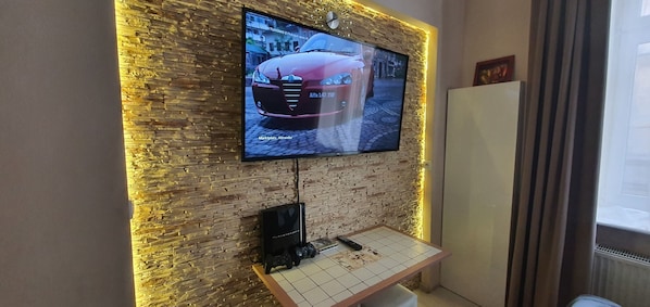 A flat-screen TV mounted on a brick wall with a wooden table in front. - Rainbow Apartments 2 (Kraków)