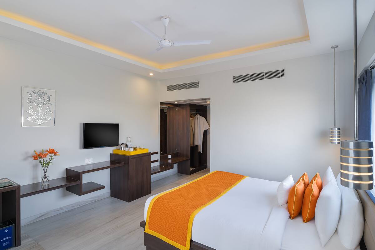 A modern hotel room with a bed, a desk, a TV, and a wardrobe.