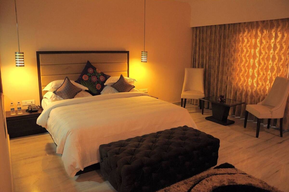 A hotel room with a large bed, two bedside tables, a chair, a desk, and a curtain.