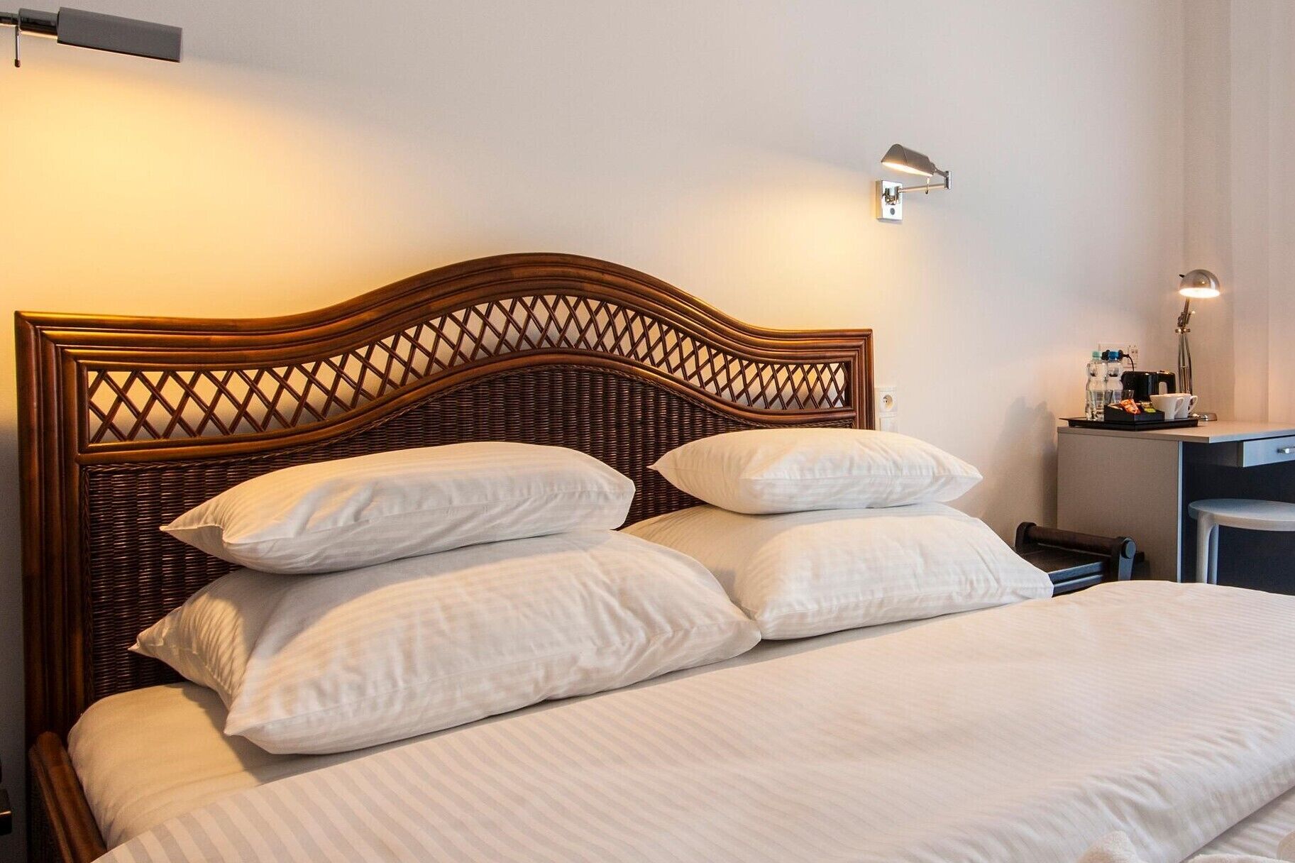 Un lit bien fait, avec une tête de lit en bois, une literie blanche et une table de chevet sur laquelle se trouvent une lampe et quelques objets.