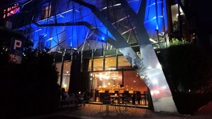 A modern building with a glass facade and blue lighting. There is a parking sign visible. - Hotel Lenart (Wieliczka)