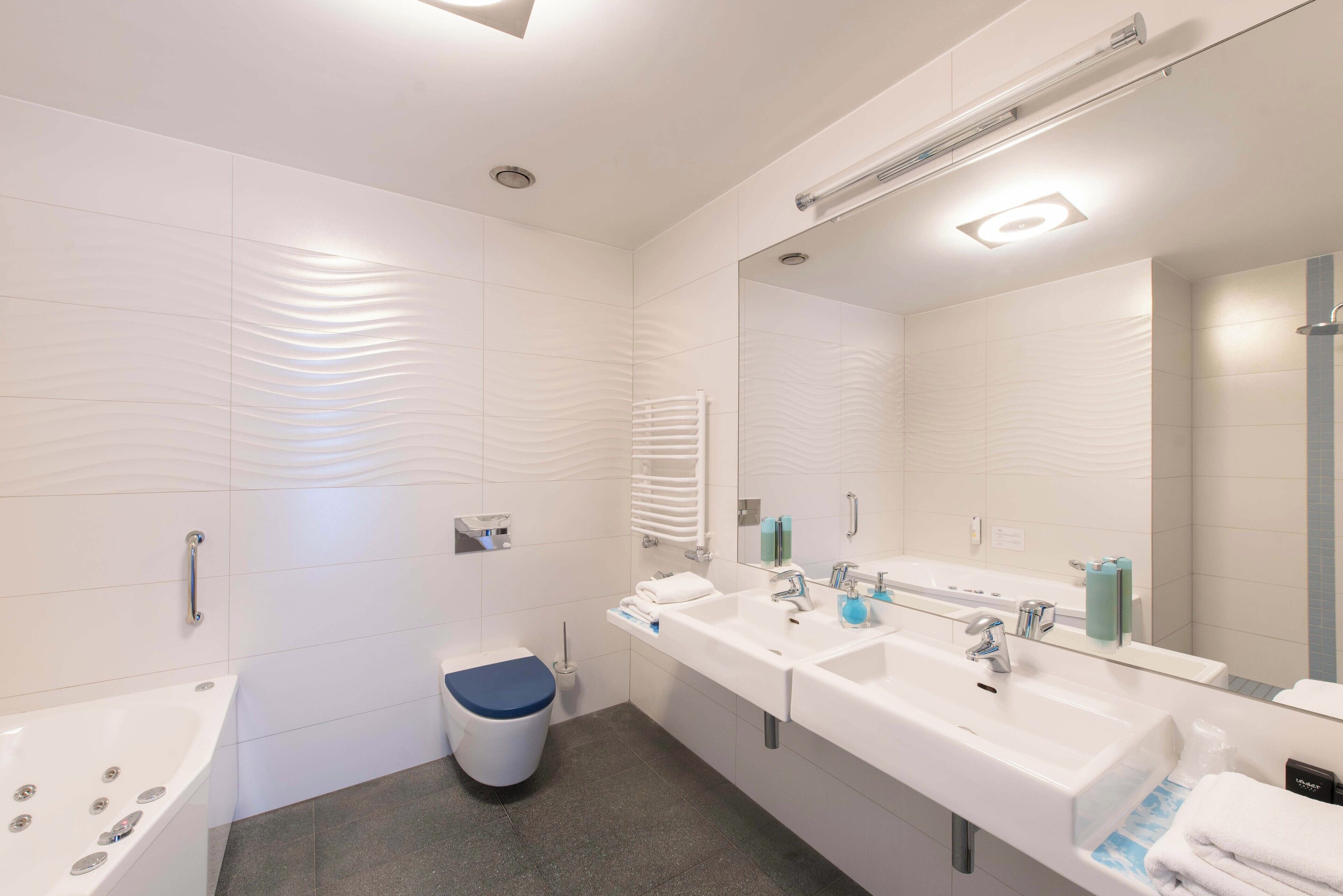 Une salle de bain moderne avec une baignoire, deux lavabos, des toilettes et un grand miroir.