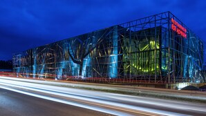 A modern building with a glass facade and a prominent red sign. - Hotel Lenart (Wieliczka)