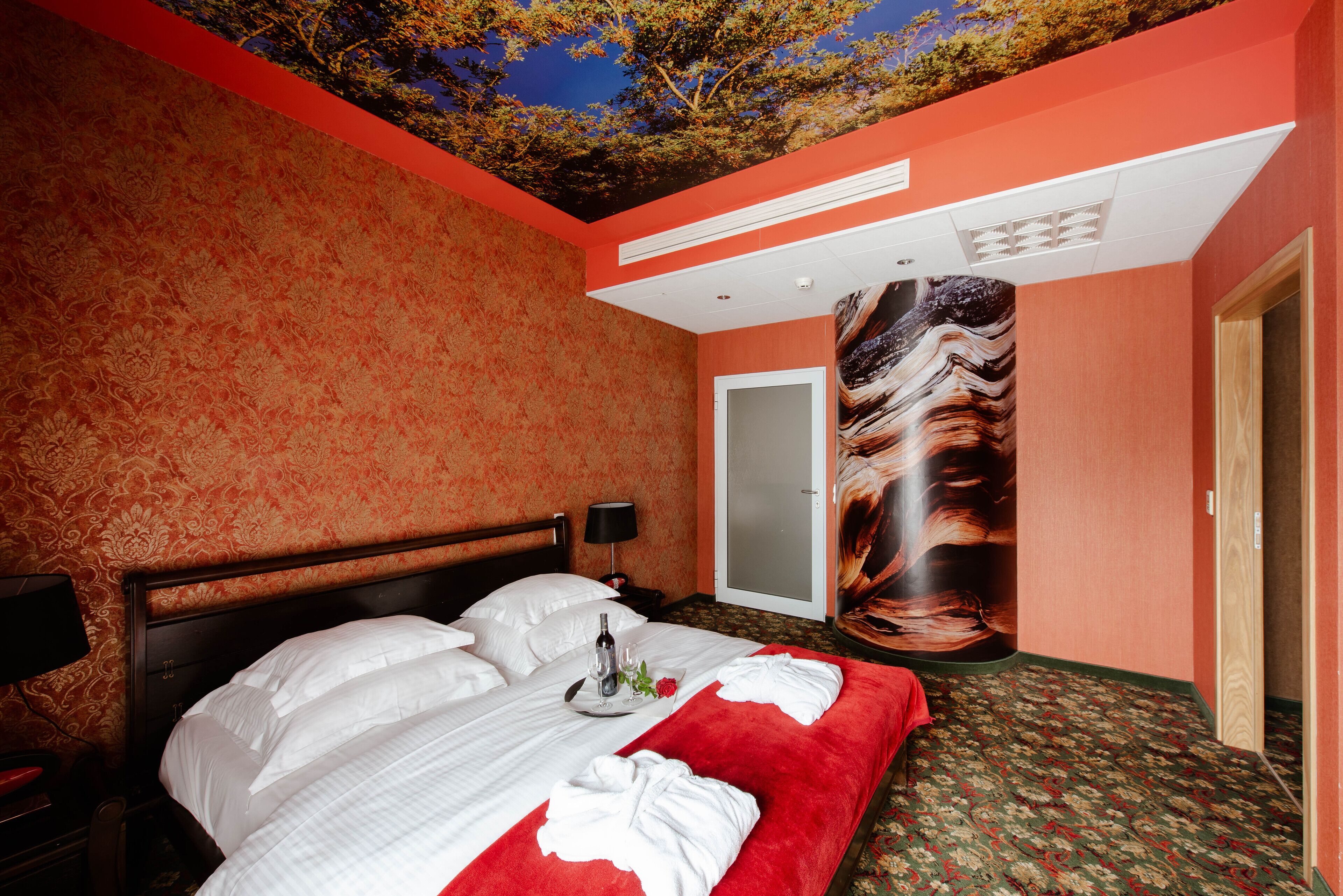 A hotel room with a large bed, a red carpet, a ceiling mural, and a door.