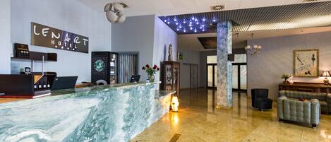Un hall d’hôtel avec un comptoir en marbre, un bureau d’accueil, une horloge et un lustre.
