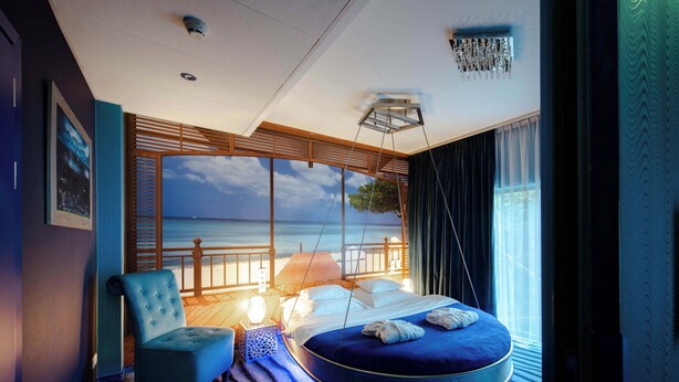 A circular bed with a view of the sea, a hanging chair, and a large window with curtains. - Hotel Lenart (Wieliczka)