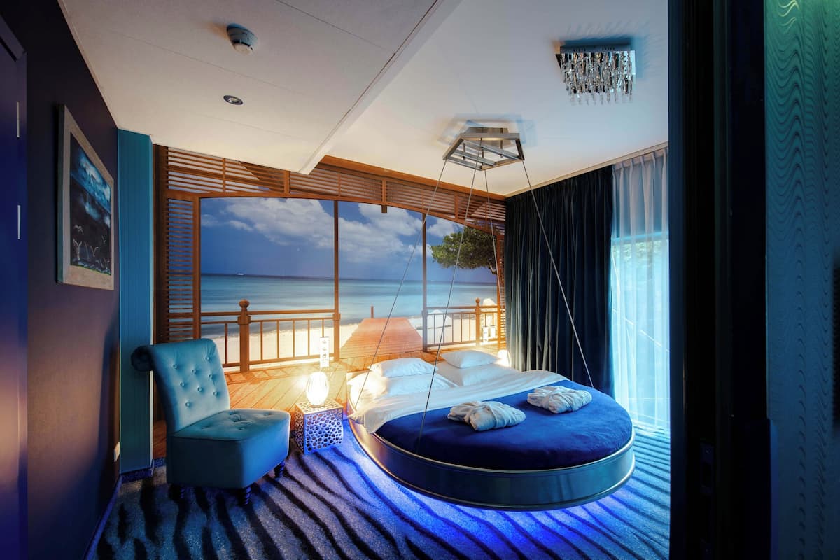 A circular bed with a view of the sea, a hanging chair, and a large window with curtains.
