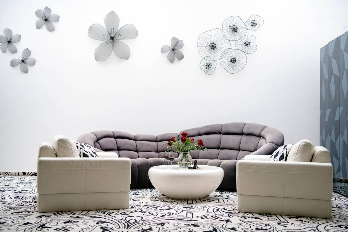 A modern living room with a grey sofa, two armchairs, a round coffee table with a vase of flowers, and decorative wall art.