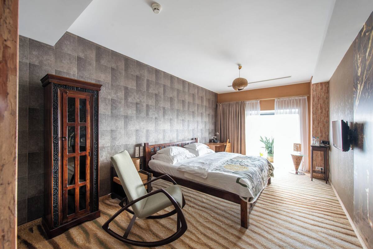 A bedroom with a large bed, a rocking chair, a wardrobe, and a television on the wall.