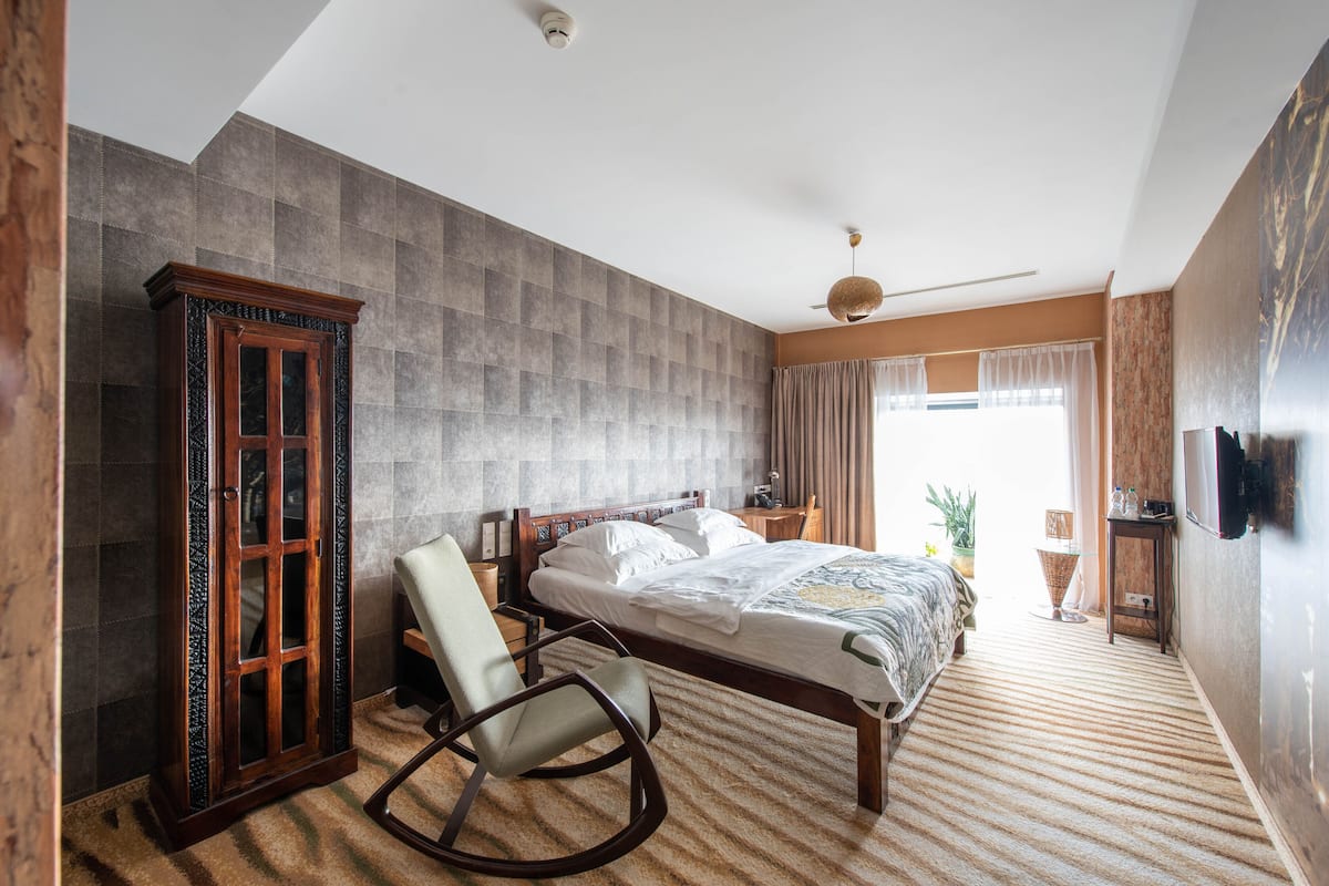 A bedroom with a large bed, a rocking chair, a wardrobe, and a television on the wall.