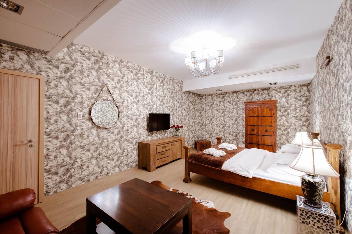 A bedroom with a wooden bed, a wooden dresser, a television, and a chandelier.