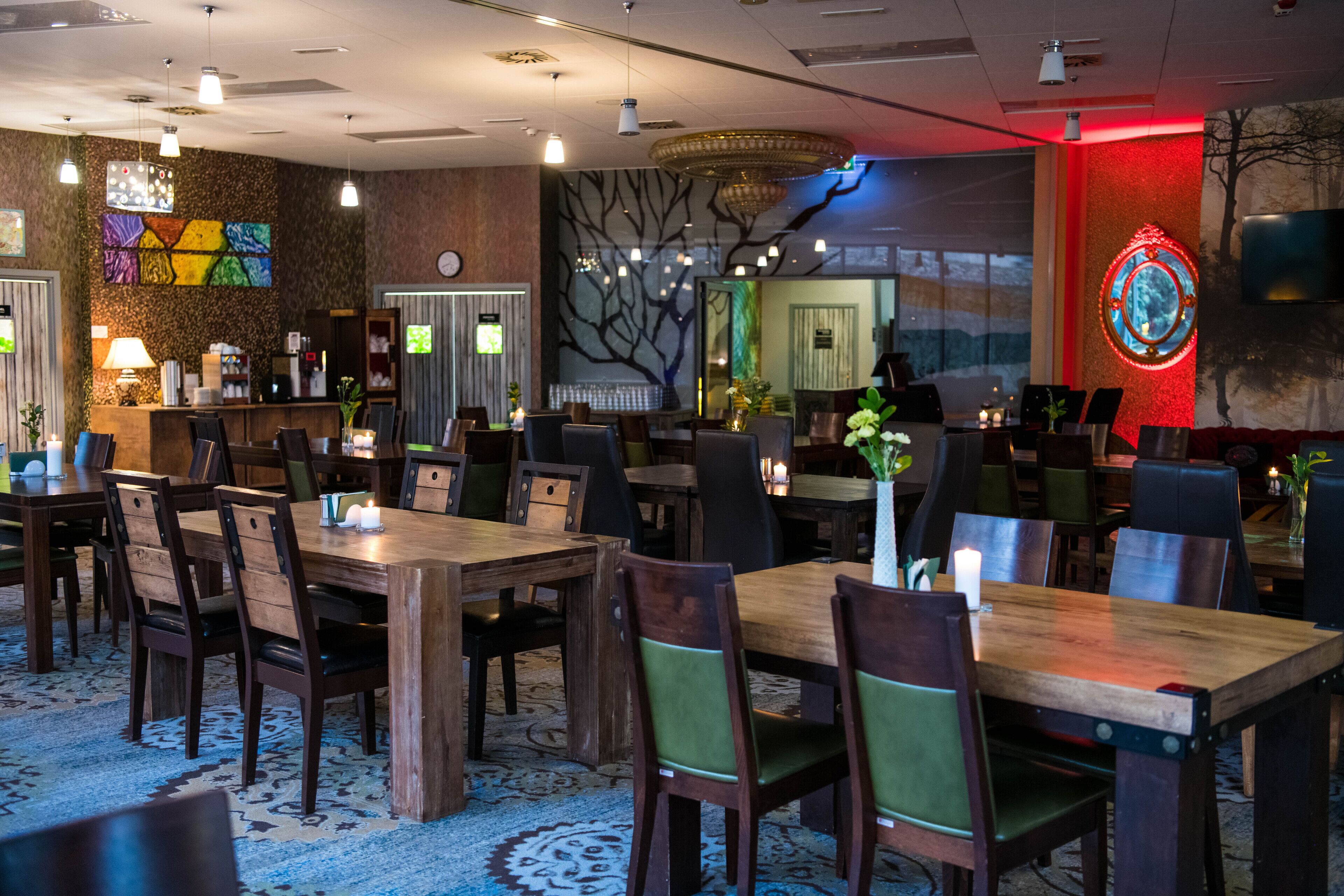 A hotel lobby with wooden tables and chairs, a reception desk, and a wall with a tree mural.