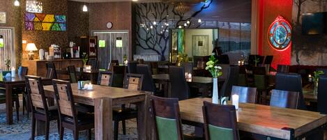 A hotel lobby with wooden tables and chairs, a reception desk, and a wall with a tree mural.