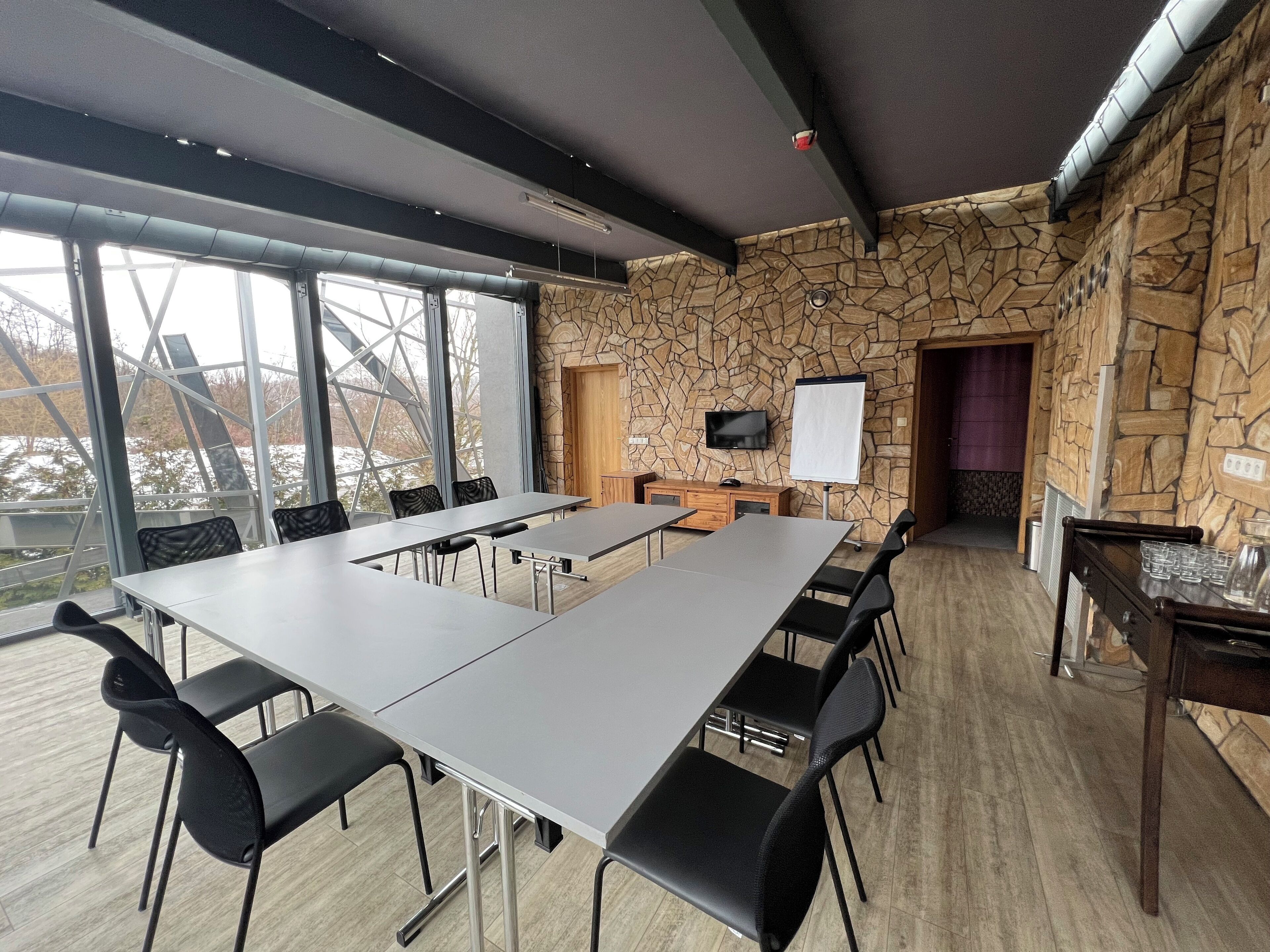 A conference room with a long table, black chairs, a stone wall, a TV, and a whiteboard.