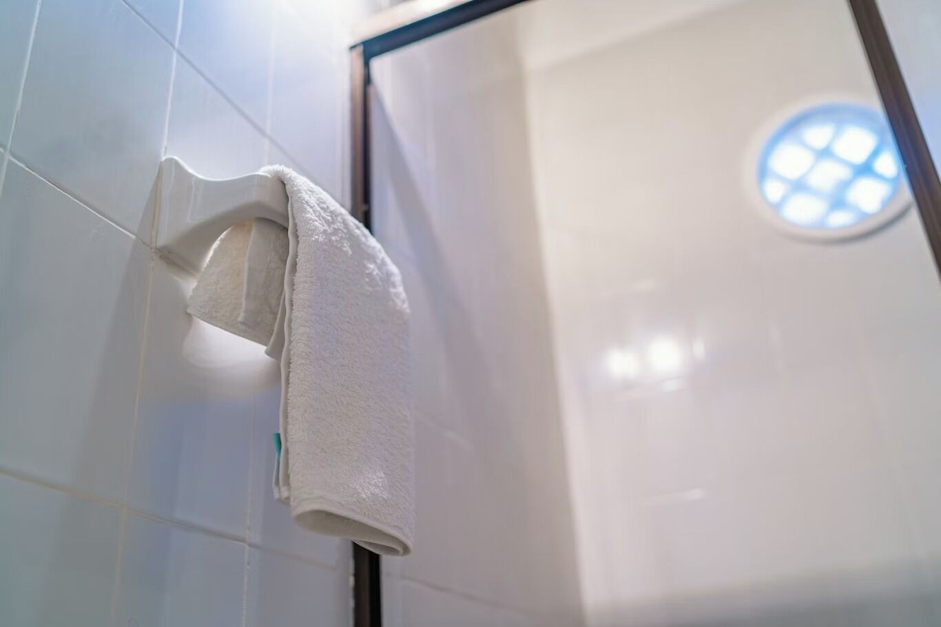A white towel hanging on a hook in a bathroom with white tiles and a circular window.