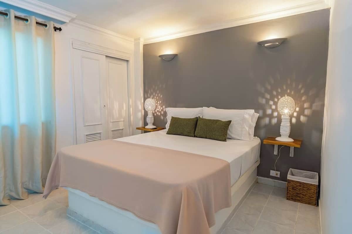 A neatly made bed with a white and beige bedspread, two pillows, and two bedside lamps on wooden nightstands.