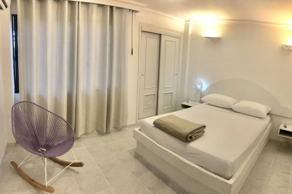 A hotel room with a bed, a chair, a nightstand, and a wardrobe.