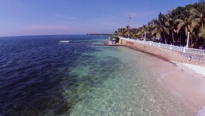 Une plage à l’eau claire, bordée d’une clôture blanche et de palmiers.