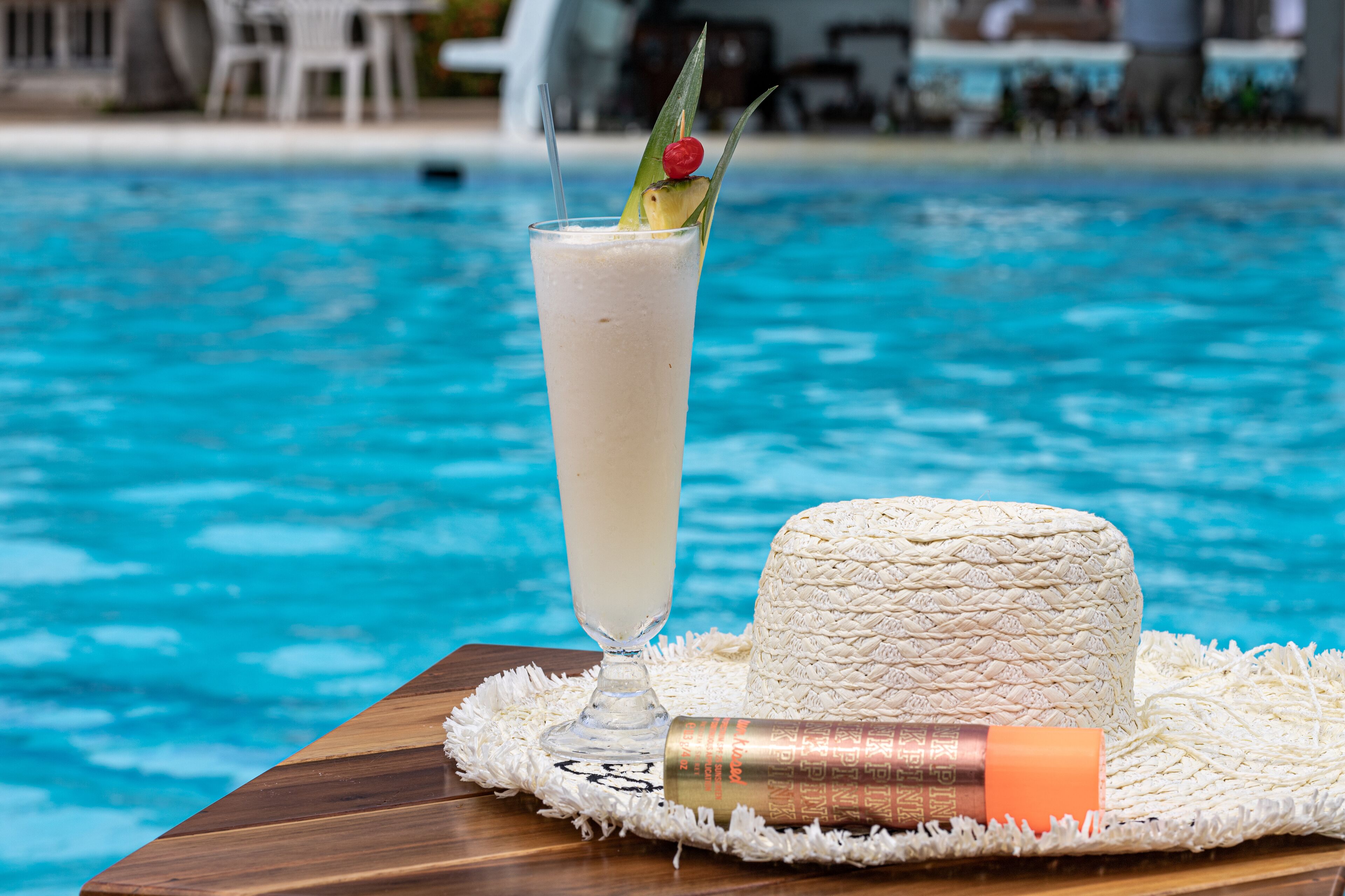A poolside setting with a drink in a tall glass, a woven mat, and a bottle.