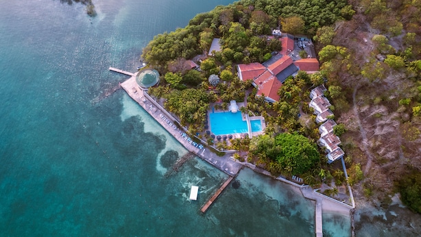 Vue aérienne d’une propriété située sur la côte, avec une piscine, un quai et une végétation luxuriante.