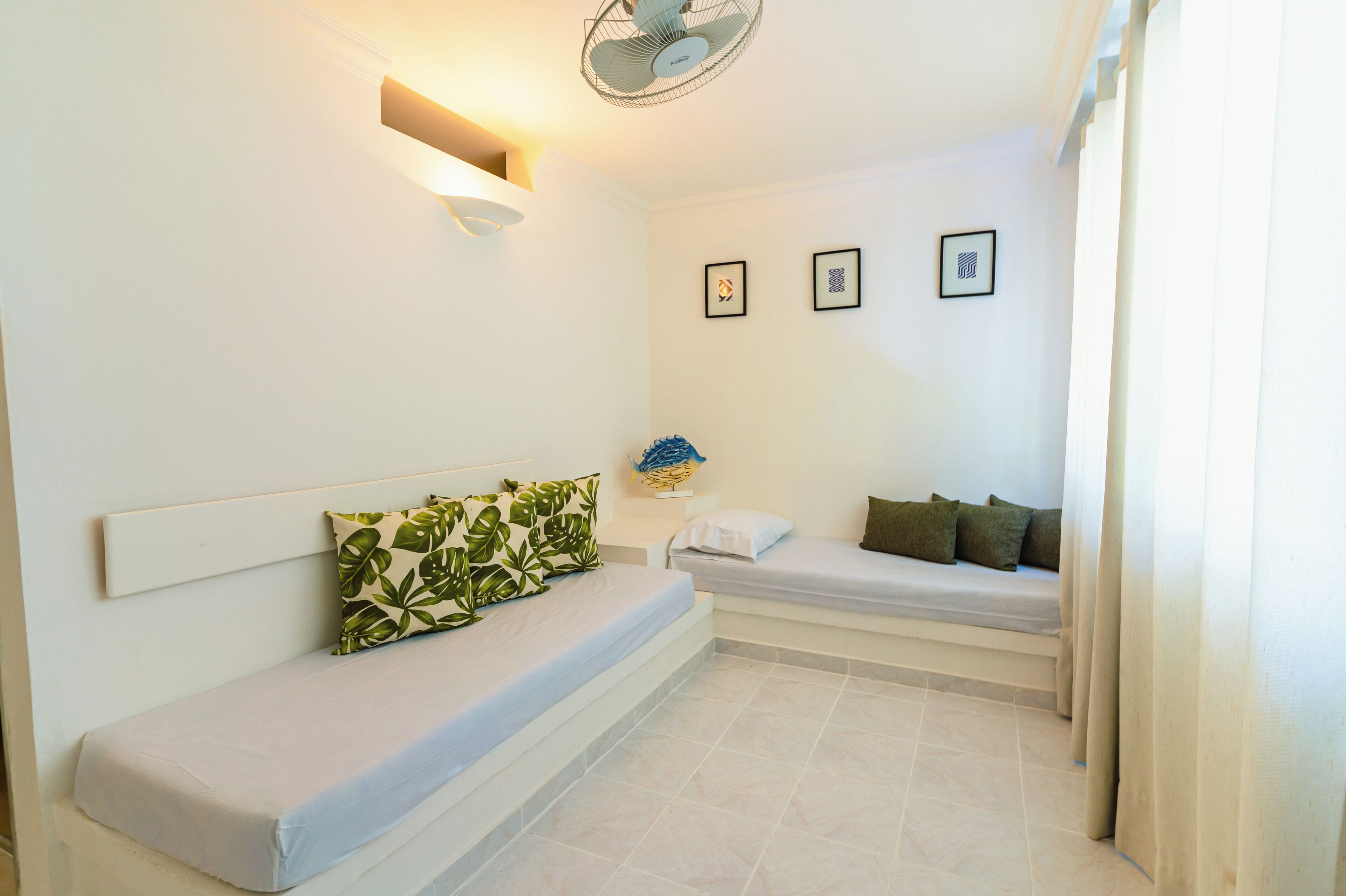 A small, clean room with two beds, a bedside table with a lamp, and a ceiling fan.