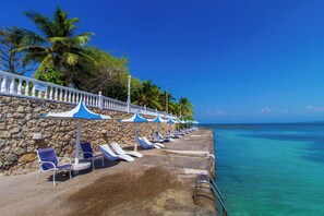 A seaside resort with a row of sun loungers and umbrellas, a stone wall, and a clear view of the ocean. - Hotel Cocoliso Island Resort (Rosario Islands)