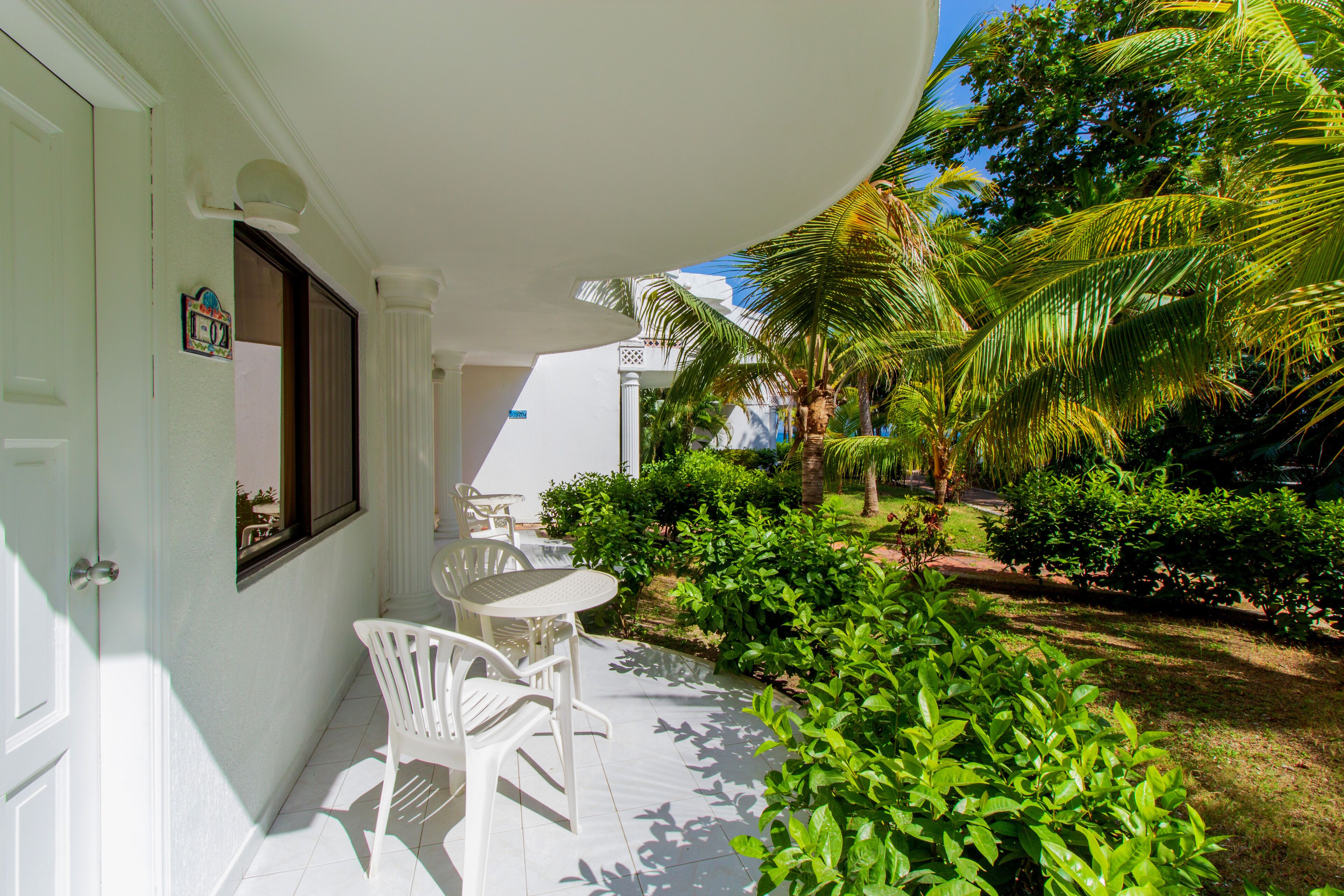 A white exterior with a covered patio, white chairs, and a small table.