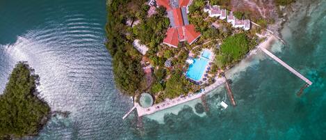 An aerial view of a tropical island with a swimming pool, a pier, and a dock.