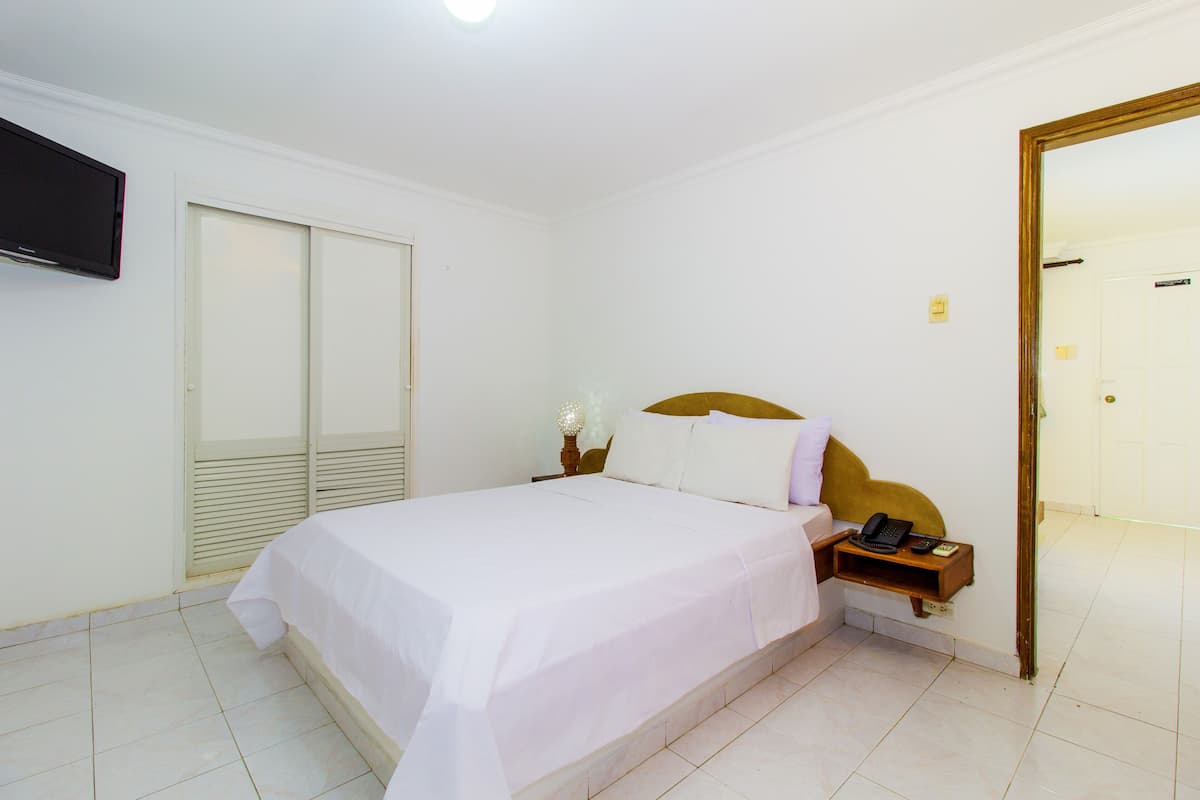 A hotel room with a large bed, a bedside table with a lamp, a TV mounted on the wall, and a sliding door closet.