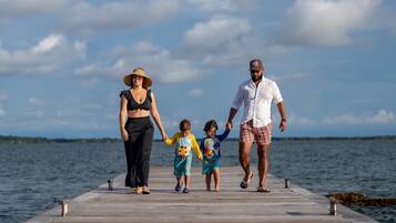A family walking on a wooden pier with a clear sky and calm sea in the background.