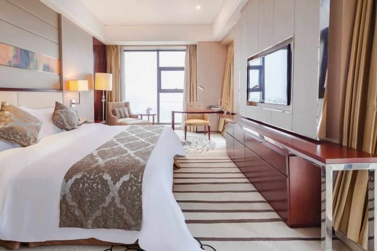 Habitación de hotel con una cama grande, un escritorio, una silla, un televisor y vistas al exterior.