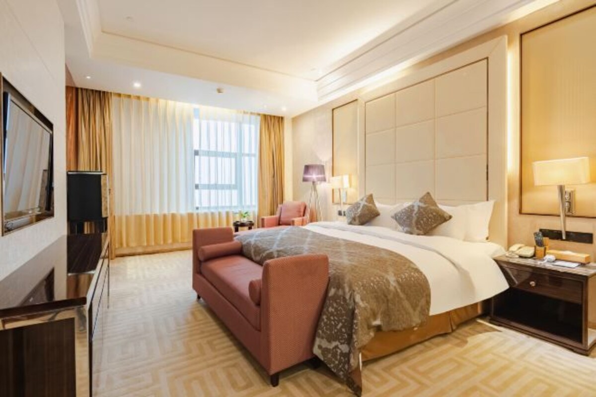 A hotel room with a large bed, a sofa, a TV, and a nightstand with a lamp.