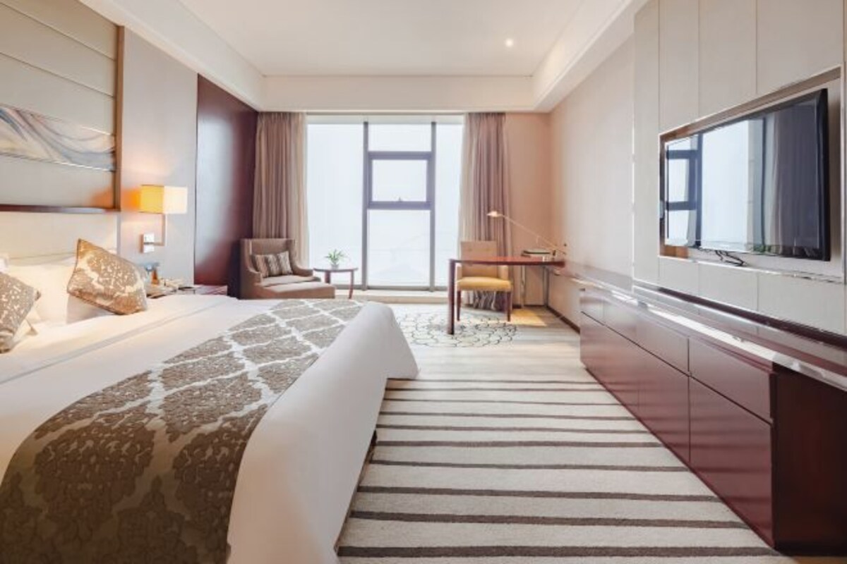A hotel room with a large bed, a desk, a chair, a TV, and a window with curtains.
