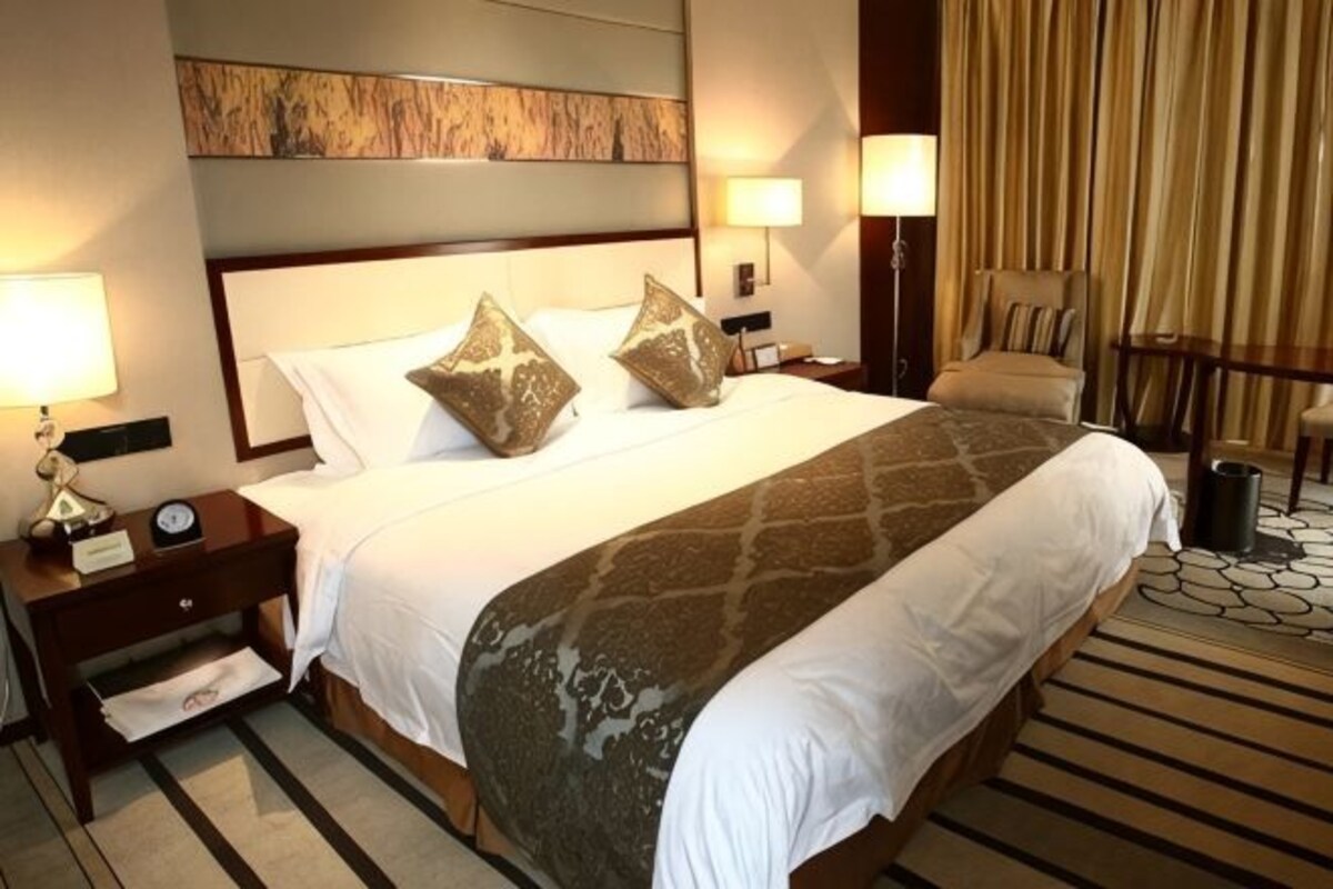 A hotel room with a large bed, two bedside tables, a chair, and a carpeted floor.