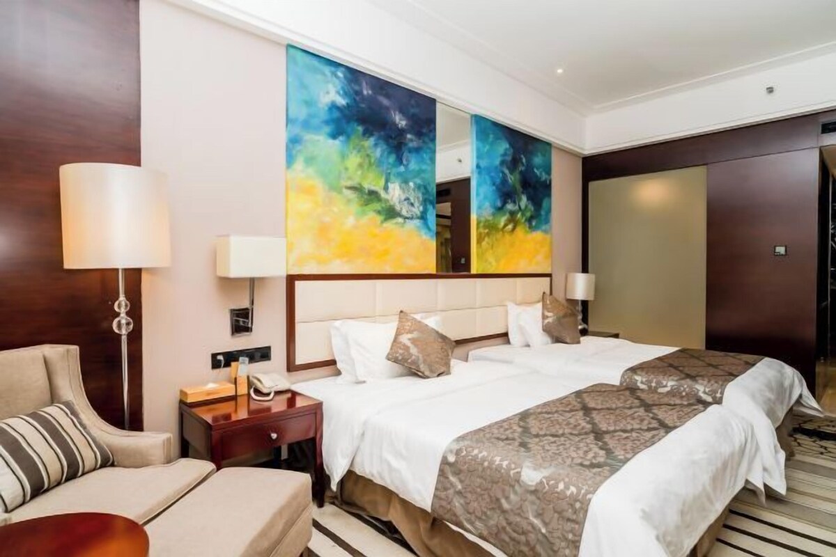 A hotel room with a large bed, a nightstand, a lamp, a sofa, and a large abstract painting on the wall.