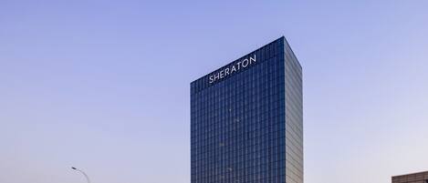 A tall, modern building with the name 'Sheraton' on its facade, surrounded by a cityscape.