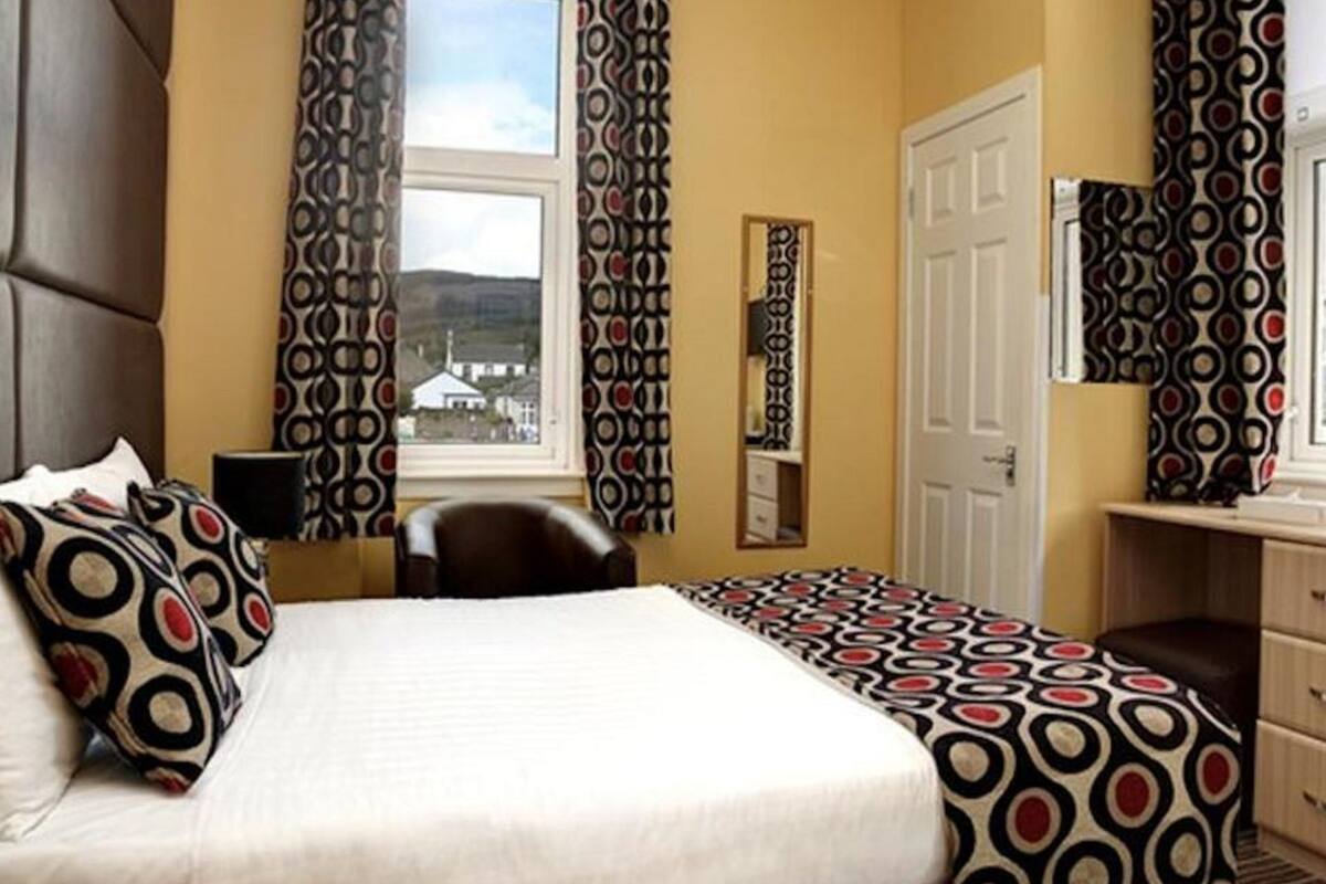 A hotel room with a large bed, a desk, a chair, and a window with curtains.
