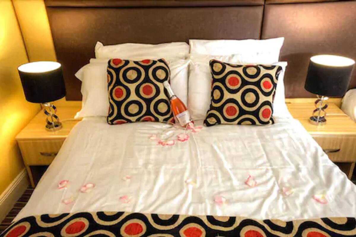 A neatly made bed with a white bedspread and two patterned pillows, flanked by two bedside lamps on wooden nightstands.