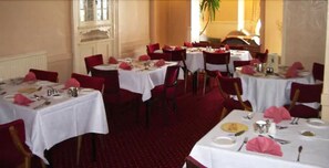 A dining area with round tables covered with white tablecloths, red chairs, and pink napkins. - The Esplanade Hotel (Dunoon)