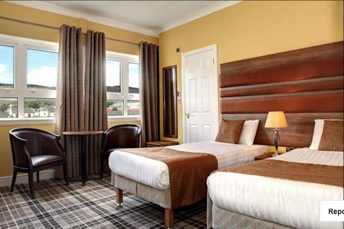 A hotel room with two beds, a chair, a small table, and a view of the outside.
