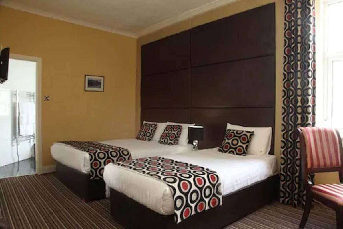 A double bed with a dark headboard, a bedside table with a lamp, and a patterned throw blanket.