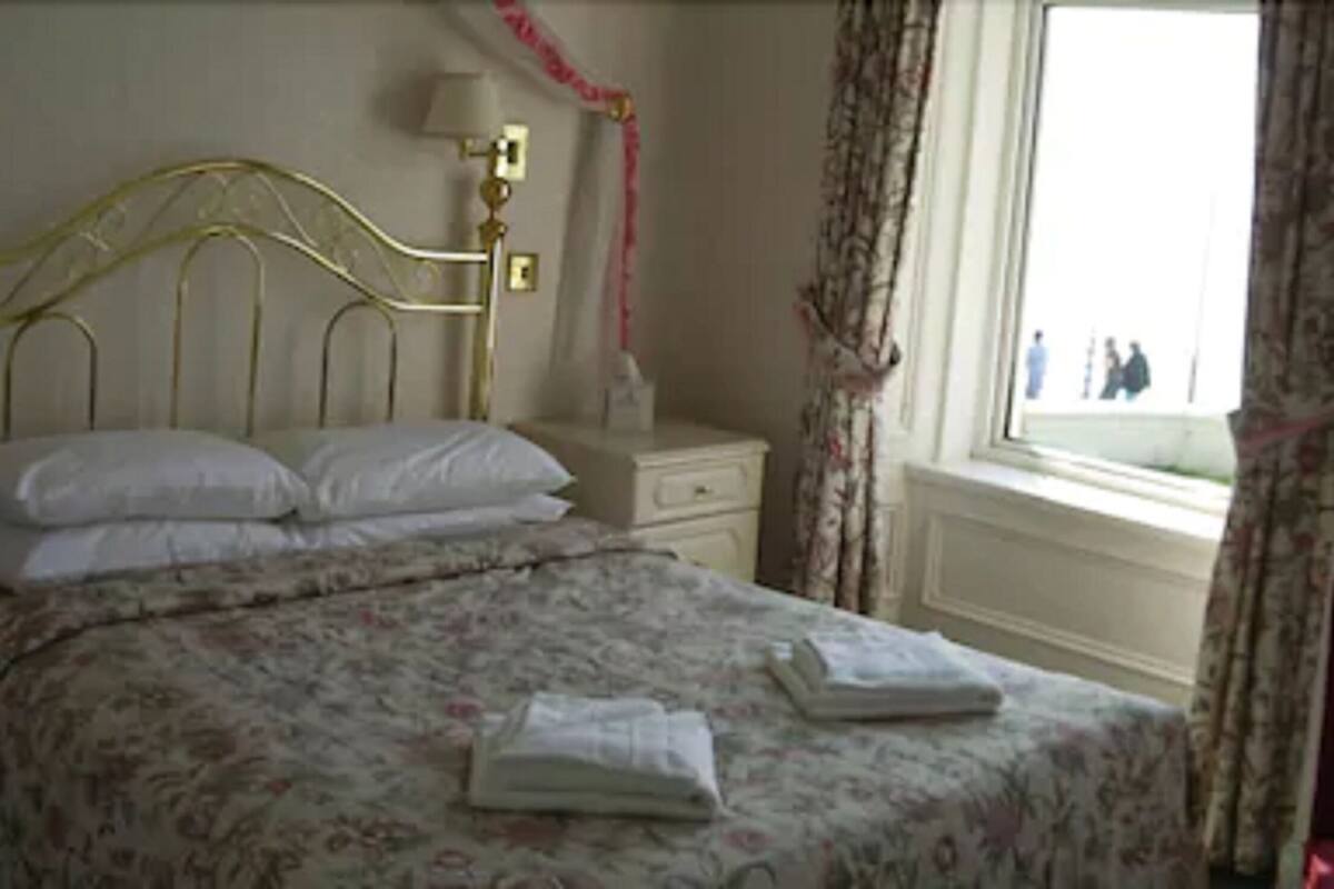 A neatly made bed with a floral bedspread, a bedside table with a lamp, and a window with curtains.