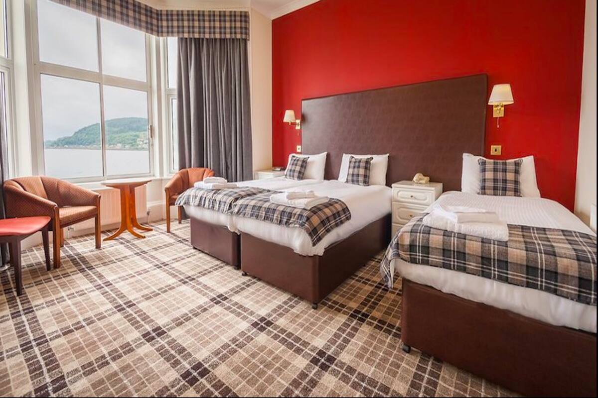 A hotel room with a large bed, two smaller beds, a chair, a table, and a view of the water.