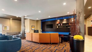 Un hall d’hôtel avec un canapé bleu, des sièges orange, un téléviseur à écran plat et une plante décorative.