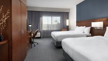 A hotel room with two beds, a desk, a chair, a wardrobe, and a large window with curtains.